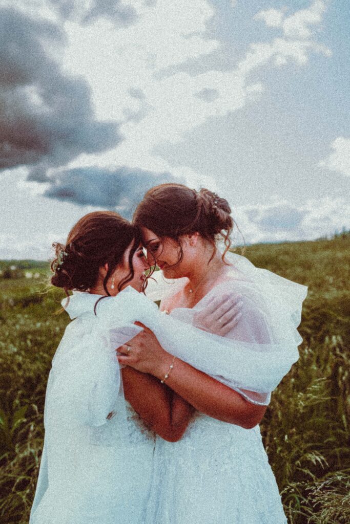 Two women in wedding dresses kissing in an open field, editorial lesbian wedding photography in Pennsylvania