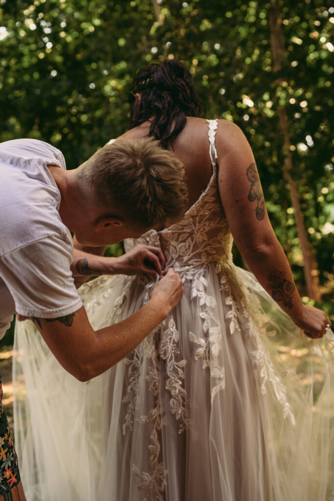 Queer partner helping their partner get dressed on their wedding day, nontraditional wedding photography